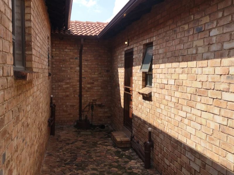 A side courtyard area featuring face brick walls, paved flooring, and a secure entrance gate, typical of a townhouse exterior utility space.