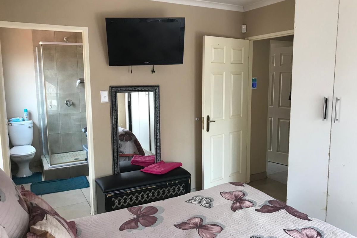 A bedroom featuring an en-suite bathroom with a glass-enclosed shower and toilet, complemented by built-in wardrobe storage.