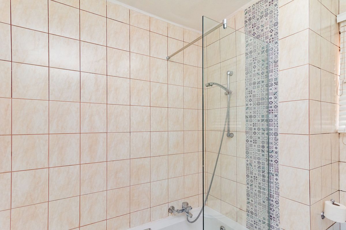 A bathroom featuring a bathtub with a glass shower screen, chrome shower fixtures, and decorative patterned accent tiling.