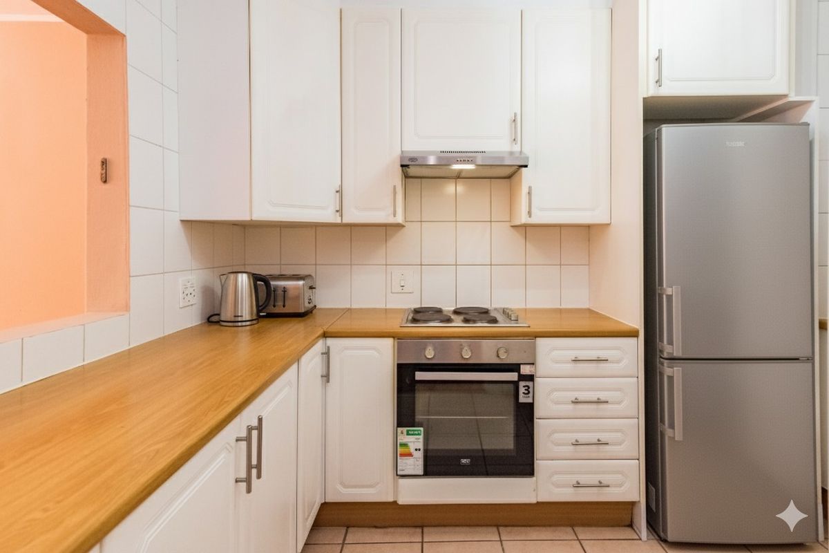 Compact kitchen featuring white cabinetry, wood-look laminate countertops, a built-in oven, electric hob, and an integrated extractor fan.