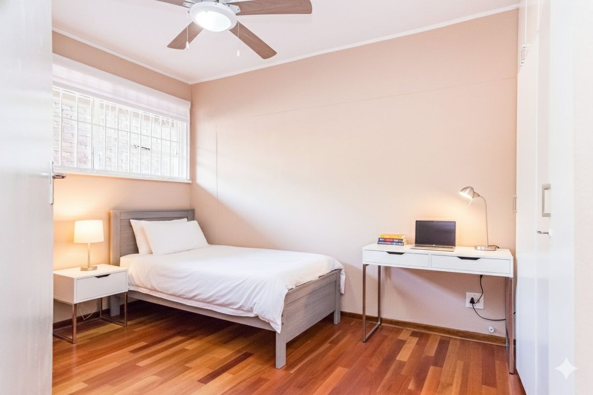 A well-maintained bedroom featuring warm-toned wooden flooring, a ceiling fan, and built-in wardrobe storage.