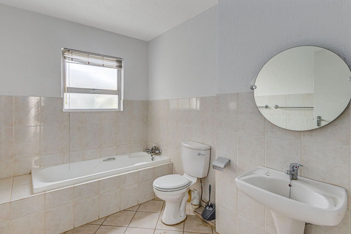 A functional bathroom featuring a built-in bathtub, pedestal sink, and toilet with neutral wall tiling and a circular wall-mounted mirror.