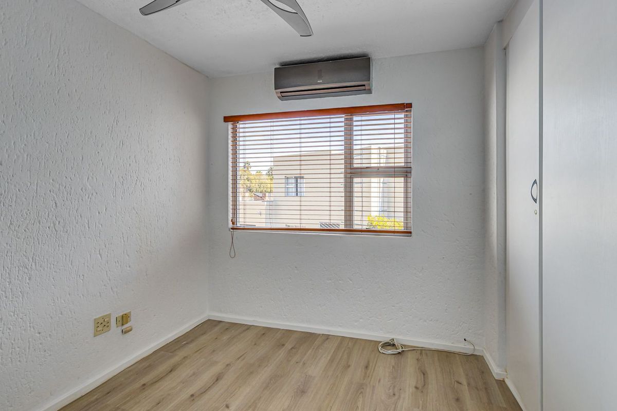 A bright, empty bedroom featuring wood-look laminate flooring, a built-in wardrobe, a ceiling fan, and a wall-mounted air conditioning unit.