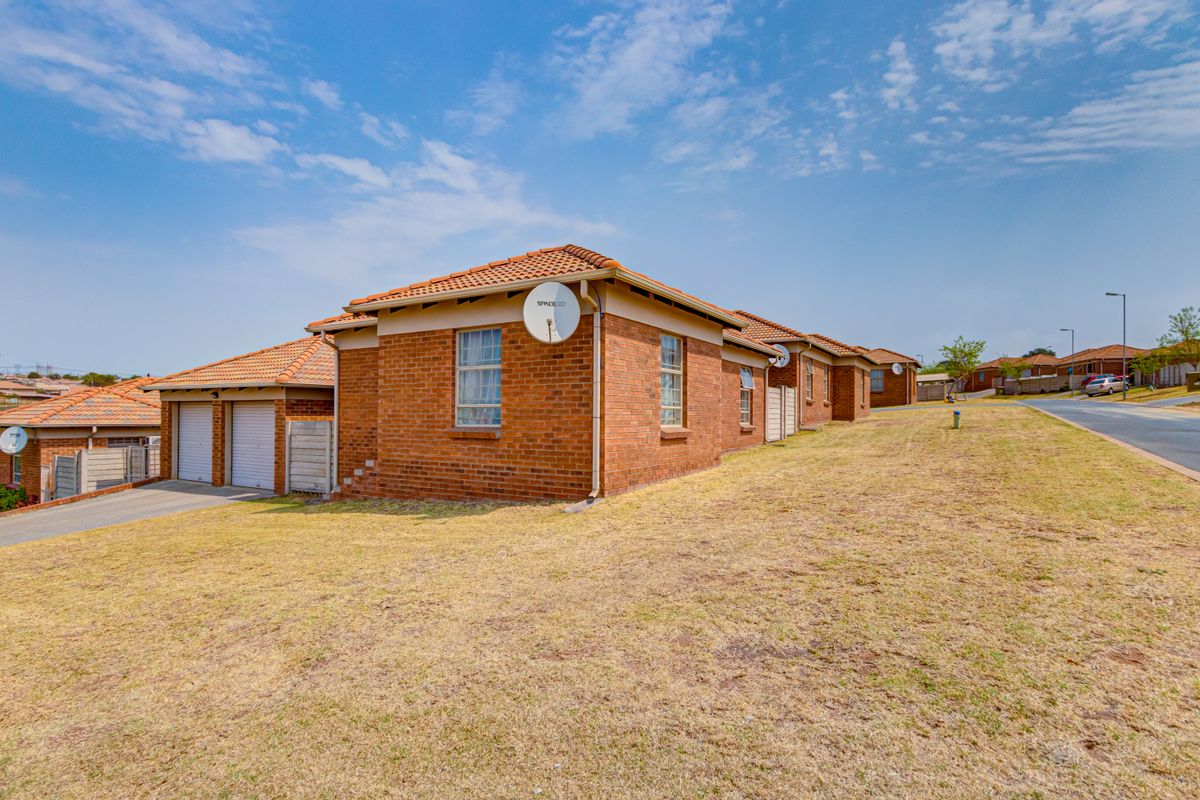 Rear view of a face brick residential property featuring a tiled roof and double garage, situated on a corner lot with an open lawn area.