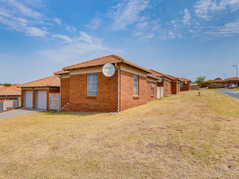 Rear view of a face brick residential property featuring a tiled roof and double garage, situated on a corner lot with an open lawn area.