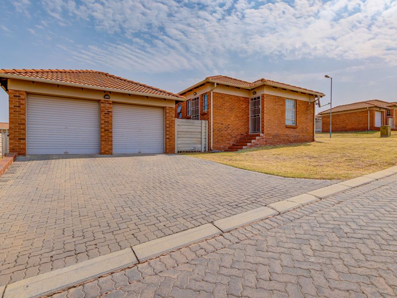 Front view of a brick-faced house featuring a double garage, paved driveway, and tiled roof in a residential estate setting.