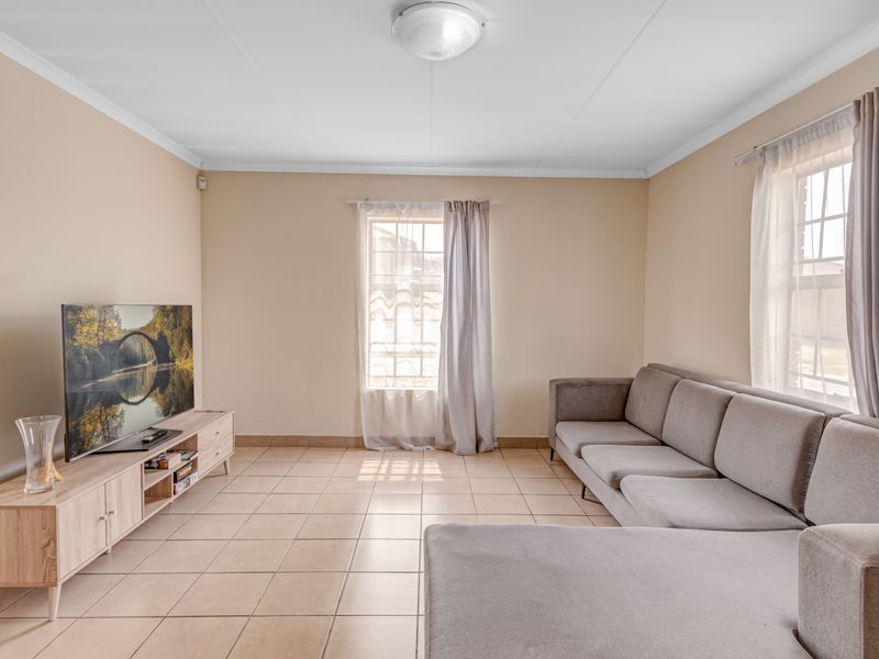 A bright living room featuring neutral wall tones, tiled flooring, and natural light from dual windows.