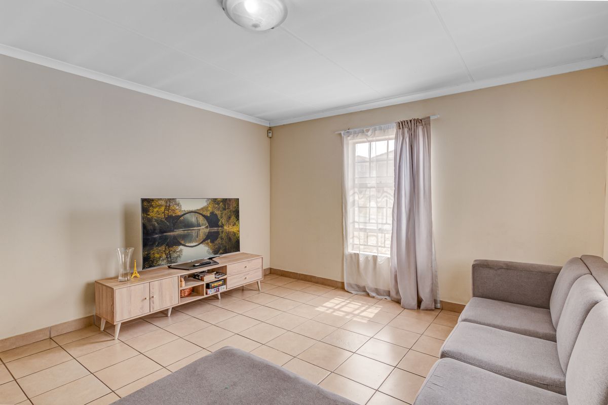 A living room featuring neutral wall tones, tiled flooring, and a window with natural light, providing a functional and well-maintained living space.