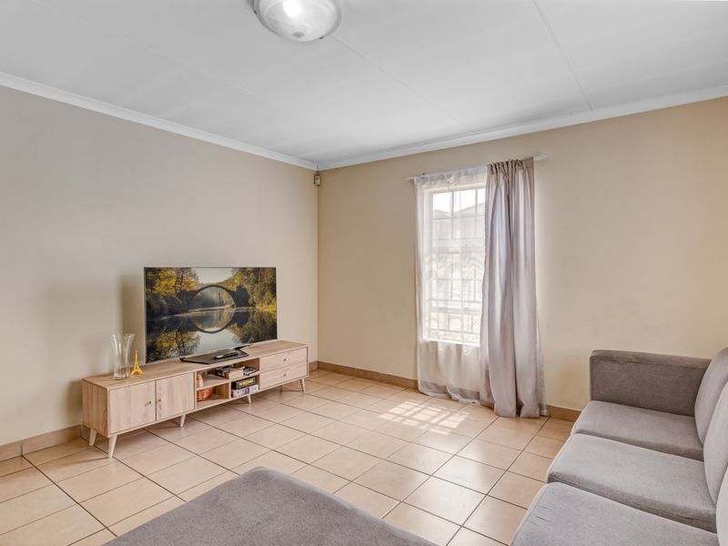 A living room featuring neutral wall tones, tiled flooring, and a window with natural light, providing a functional and well-maintained living space.