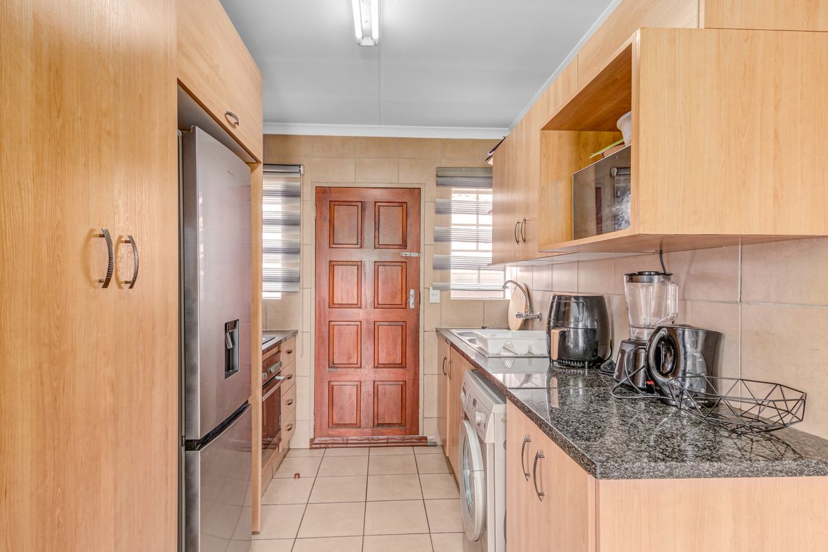 A functional galley-style kitchen featuring light wood cabinetry, granite countertops, tiled backsplash, and integrated appliance spaces with direct access to an exterior door.