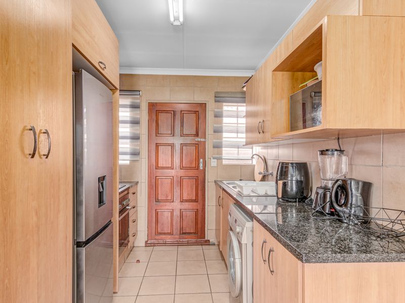 A functional galley-style kitchen featuring light wood cabinetry, granite countertops, tiled backsplash, and integrated appliance spaces with direct access to an exterior door.
