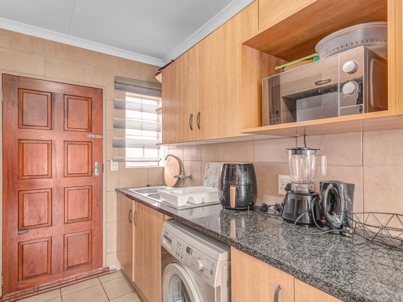 Functional scullery featuring laminate cabinetry, granite countertops, stainless steel sink, and integrated microwave shelf with tiled finishes.