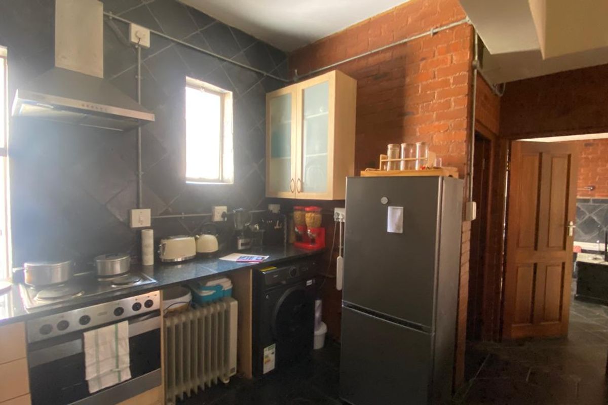 A kitchen featuring exposed brick walls, dark tiled splashbacks, built-in cabinetry, a stainless steel extractor fan, and a freestanding stove.