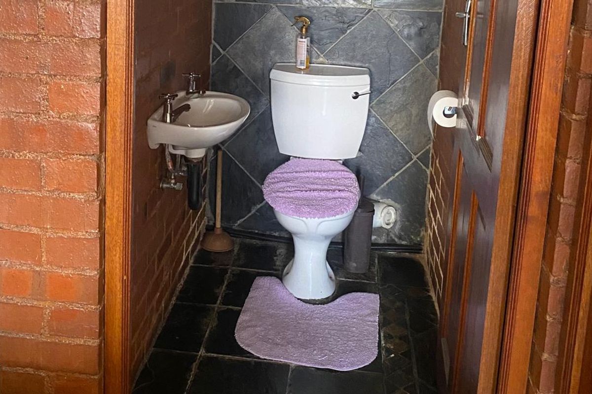 A compact guest bathroom featuring a wall-mounted basin and toilet, finished with exposed brick walls and dark slate tiling.