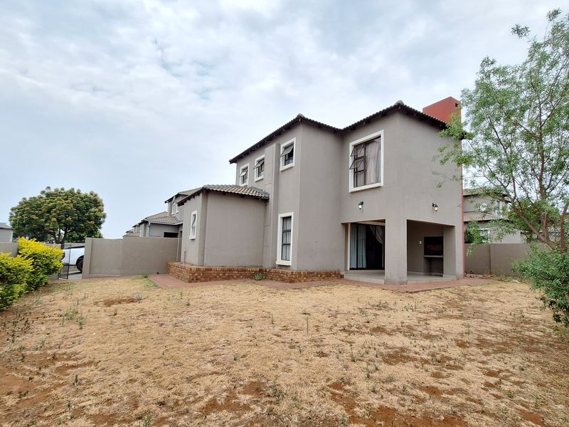 Rear view of a double-story house featuring a covered patio with a built-in braai, overlooking a private garden with boundary walling.