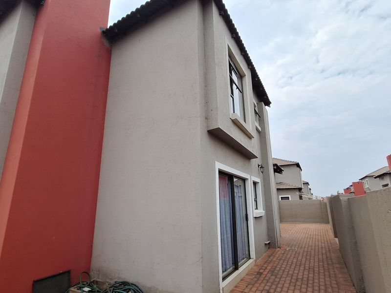 A side view of the property showing a paved walkway, sliding door access, and exterior wall finishes with a tiled roof.
