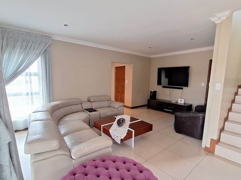 A spacious living room featuring neutral tiled flooring, recessed downlighting, and a staircase leading to the upper level.