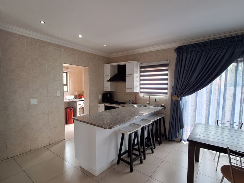 Open-plan kitchen and dining area featuring granite countertops, built-in cabinetry, tiled flooring, and direct access to a separate scullery or laundry space.