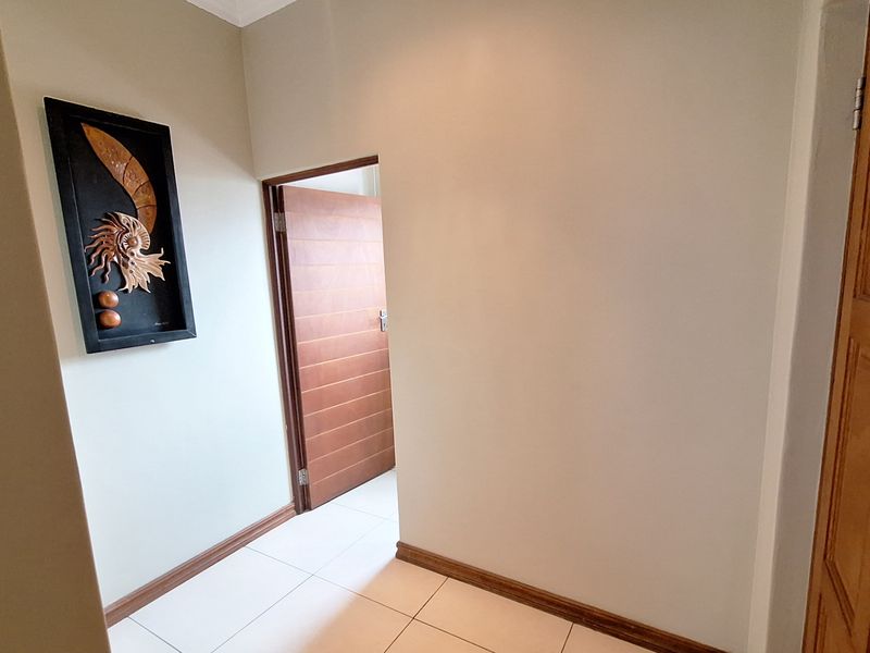 A clean and well-maintained hallway featuring neutral wall tones, tiled flooring, and timber door finishes.