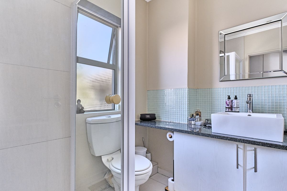 A modern bathroom featuring a vanity with a granite countertop, a vessel sink, a wall-mounted mirror, and a separate toilet area.