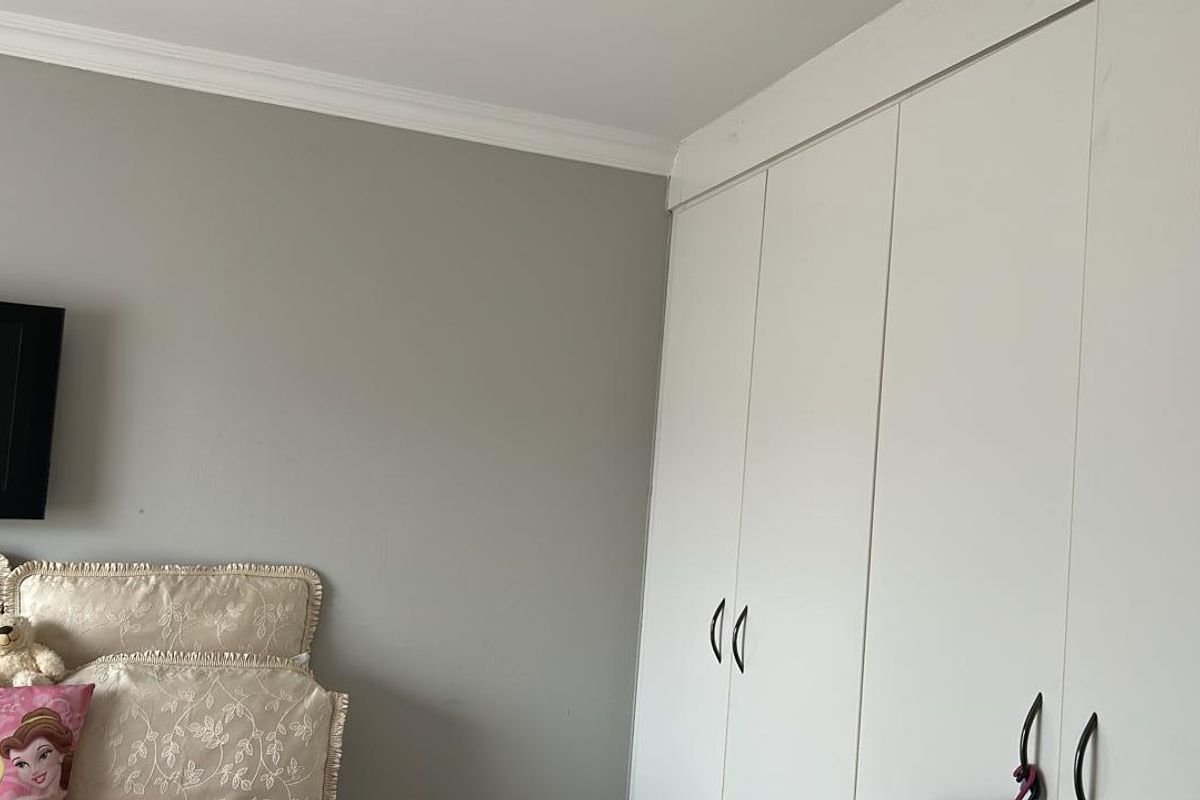 A bedroom featuring built-in white cabinetry with modern handles and crown molding detail.