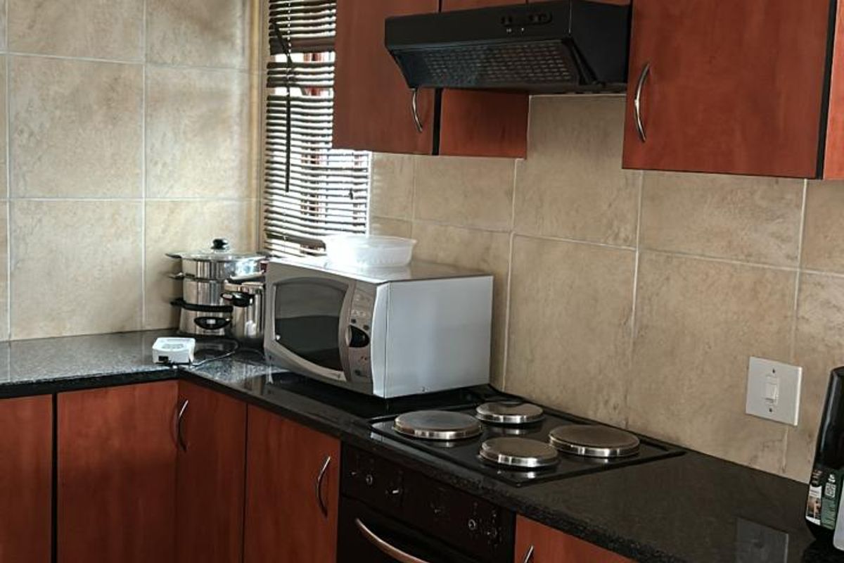 A functional kitchen featuring dark wood cabinetry, granite countertops, tiled splashbacks, and integrated electric oven and hob with an extractor fan.