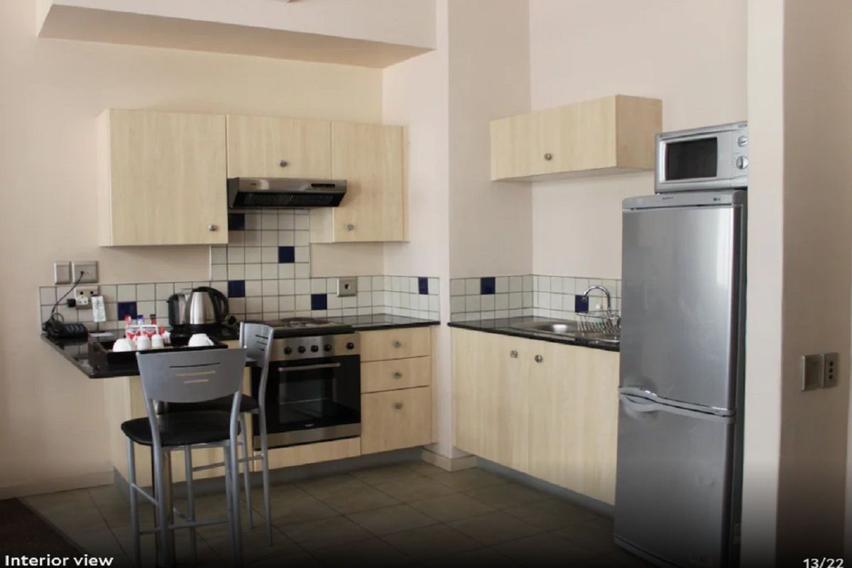 Compact kitchen featuring light wood cabinetry, dark countertops, tiled backsplash, built-in oven, hob, and extractor fan, with space for a refrigerator.
