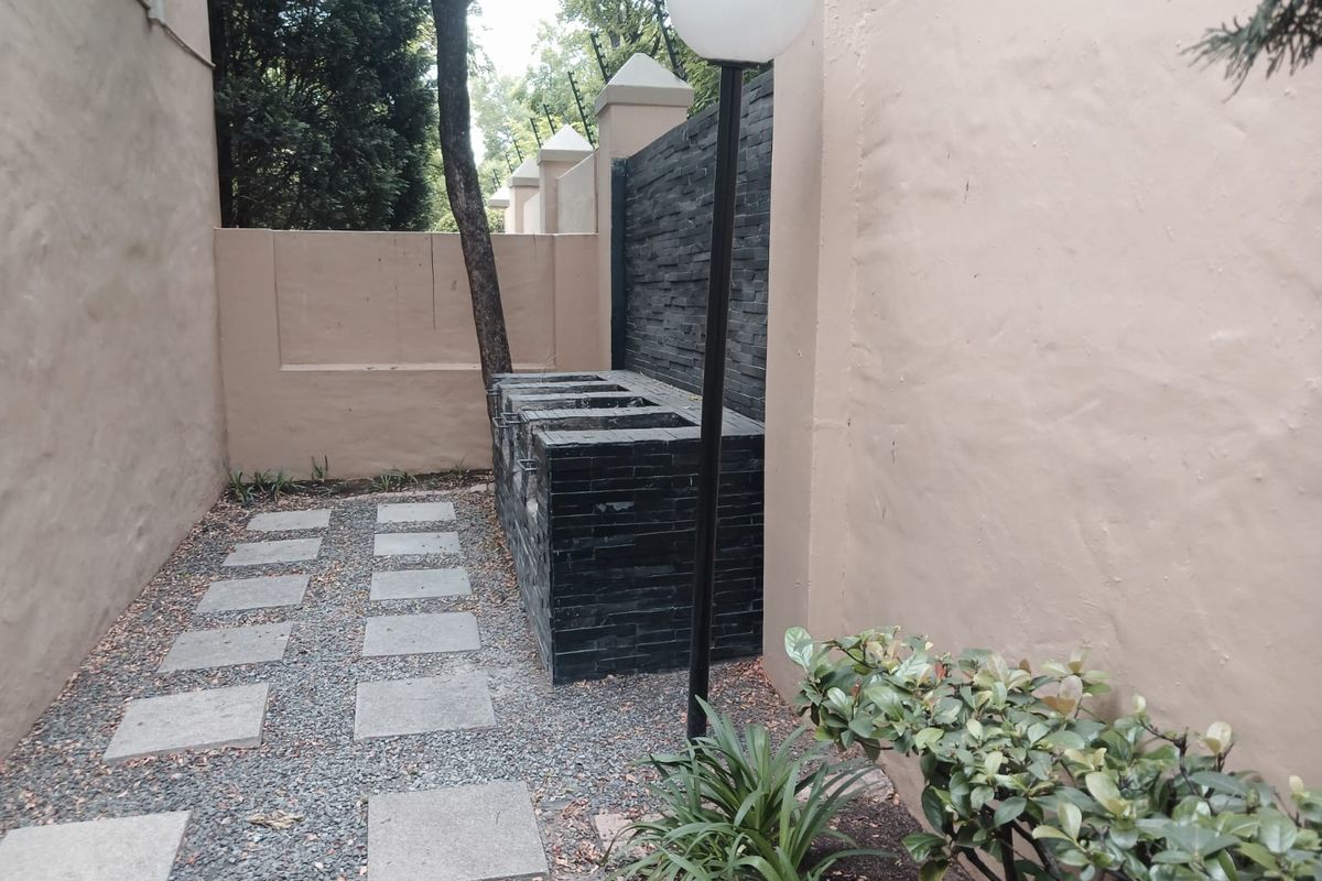 Outdoor area featuring a built-in stone braai or barbecue station, paved walkway, and high boundary walls with security spikes.