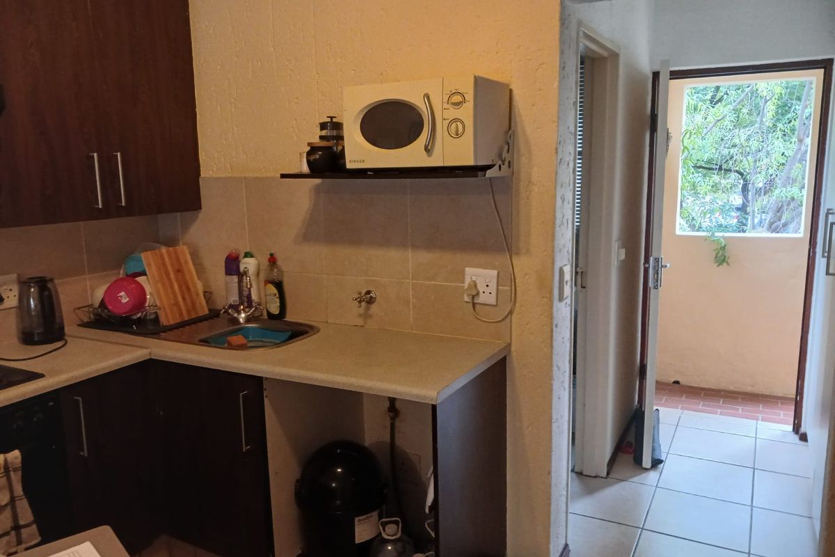 Compact kitchen area featuring dark cabinetry, tiled backsplash, and a stainless steel sink, with direct access to an outdoor balcony area.
