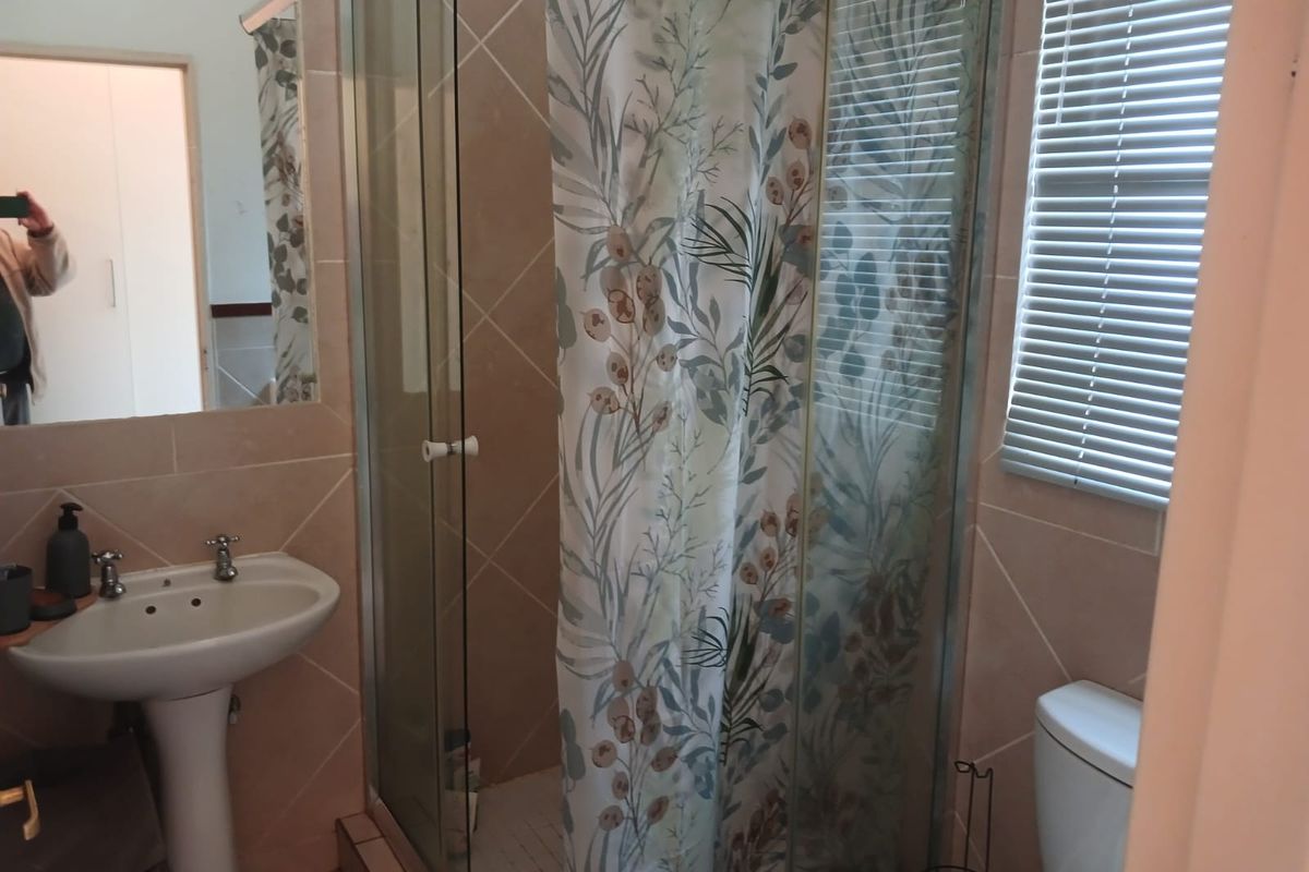 A functional bathroom featuring a pedestal basin, a glass-enclosed shower with tiled walls, and a toilet, complemented by natural light from a window.