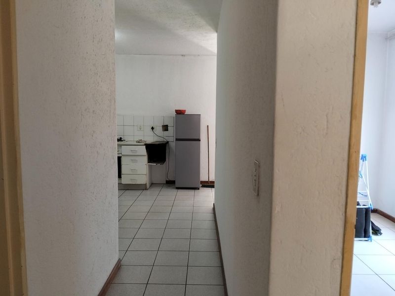A view through a hallway into a functional kitchen area featuring tiled flooring, built-in cabinetry, and a tiled backsplash.