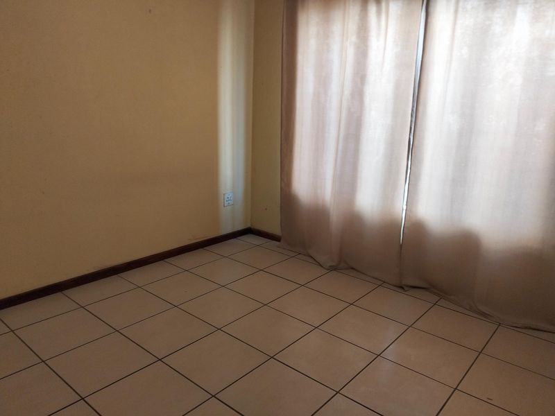 An empty bedroom featuring neutral ceramic floor tiles, plain walls, and window curtains, offering a blank canvas for personalization.