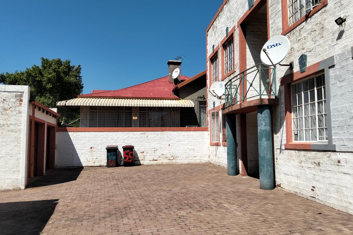 Rear courtyard area featuring brick paving, a boundary wall, and access to an upper-level balcony with satellite dish installations.