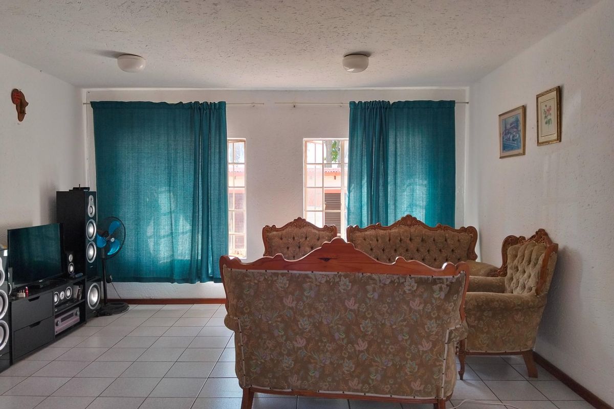 A living room featuring ceramic floor tiles and dual windows with curtains, providing a functional space with neutral wall finishes.