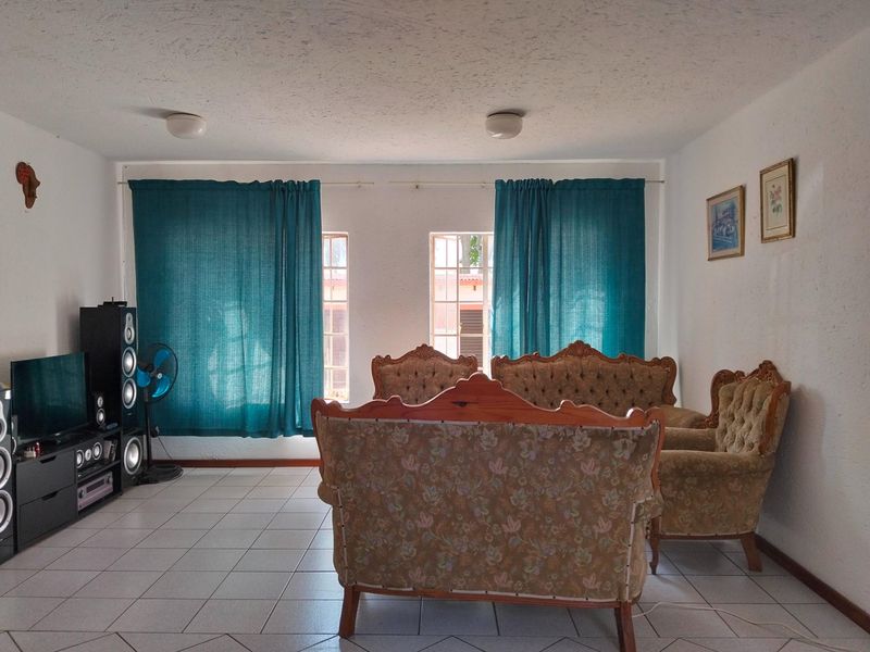 A living room featuring ceramic floor tiles and dual windows with curtains, providing a functional space with neutral wall finishes.