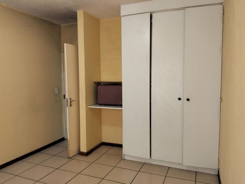 A bedroom featuring tiled flooring and a built-in wardrobe with additional open shelving, presenting a blank canvas for potential interior updates.