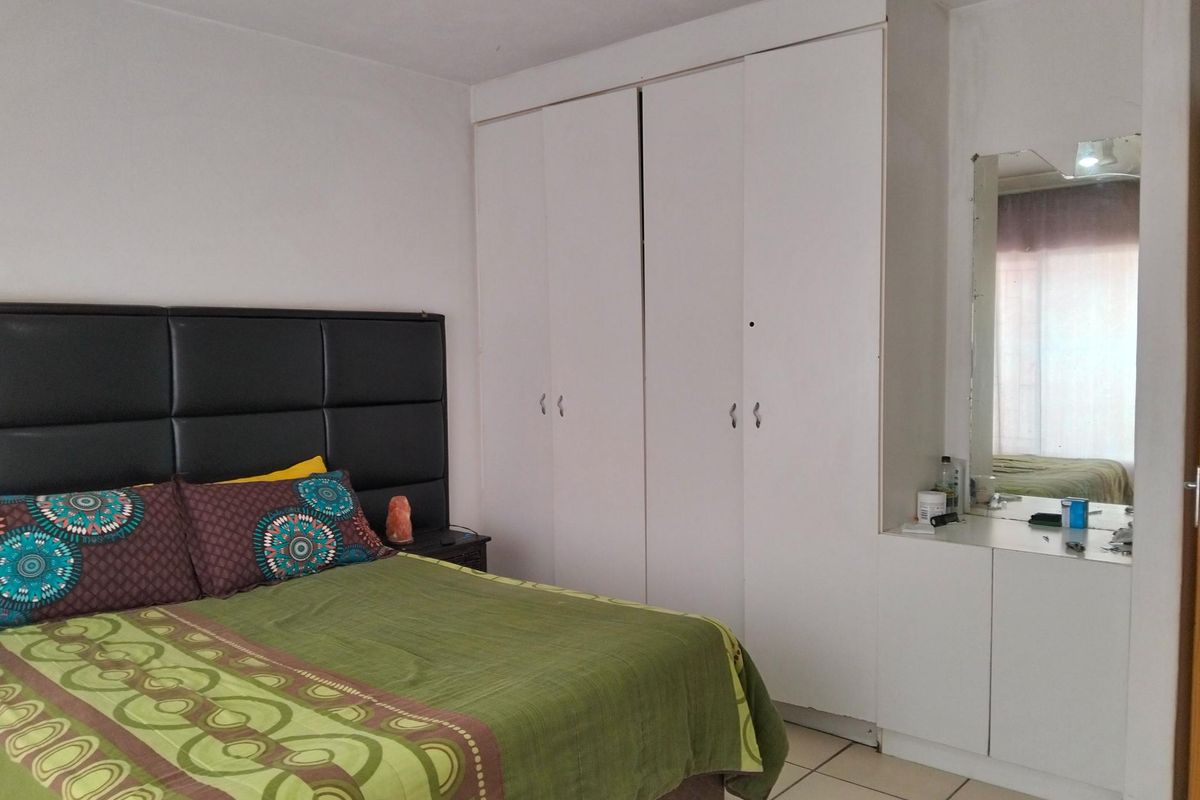 A bedroom featuring built-in white wardrobes and a vanity area with a mirror, finished with neutral floor tiles.