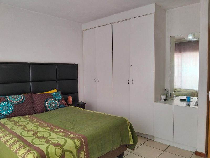 A bedroom featuring built-in white wardrobes and a vanity area with a mirror, finished with neutral floor tiles.