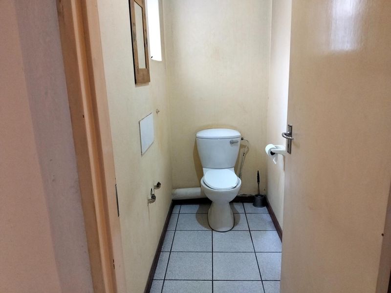 A compact, functional bathroom featuring a standard toilet, tiled flooring, and exposed plumbing connections, requiring cosmetic updates to improve its overall condition.
