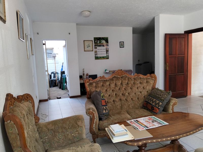 A living room area featuring tiled flooring and a wooden door, providing access to an adjacent outdoor space.