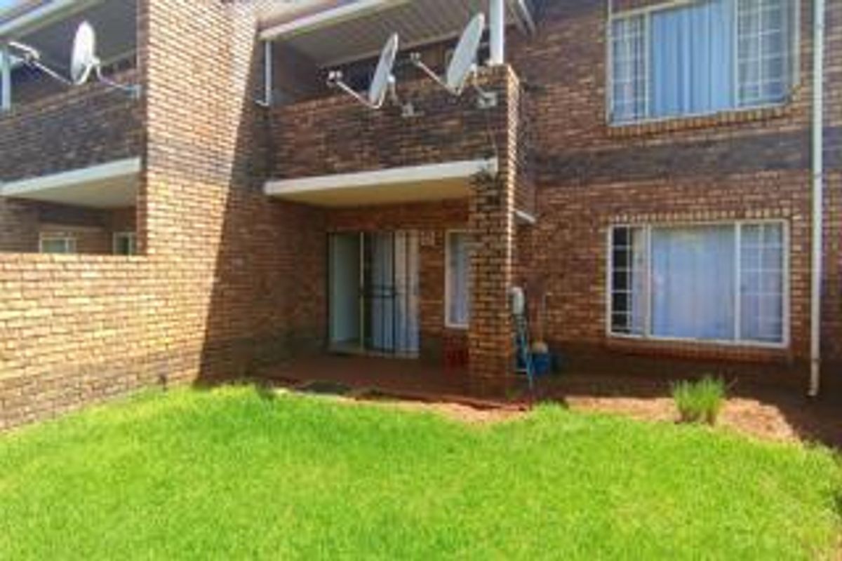 Rear view of a multi-story apartment building featuring face-brick facade, private ground-floor patio area, and small garden space.