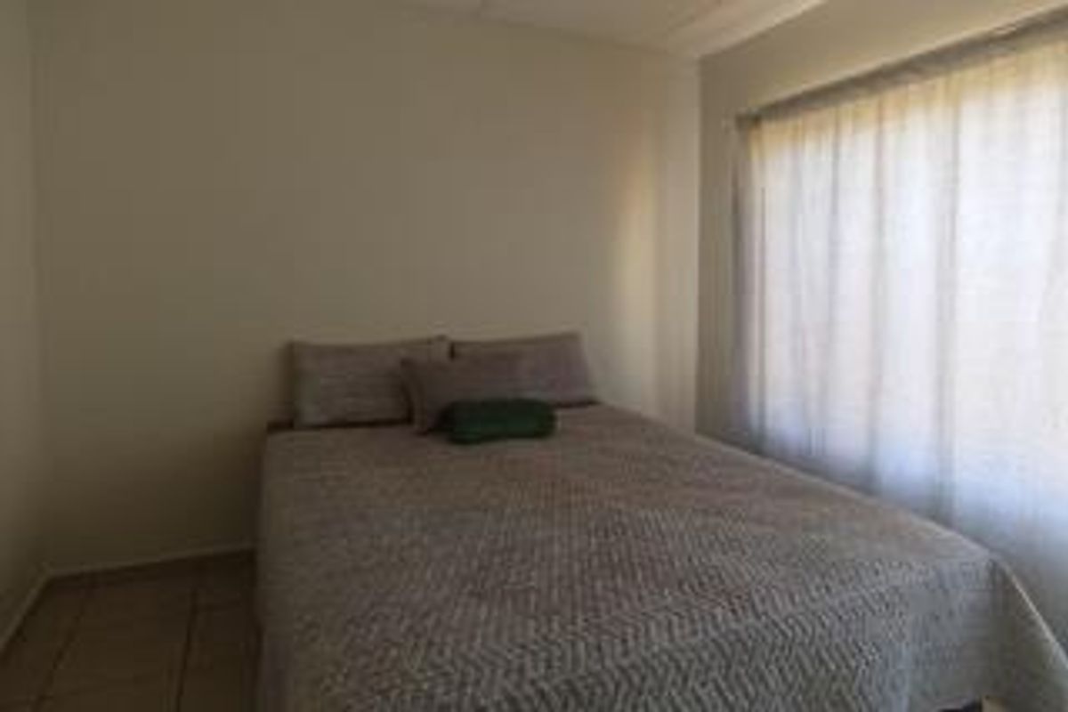 A simple bedroom featuring tiled flooring and a large window with curtains, providing a neutral and functional space.