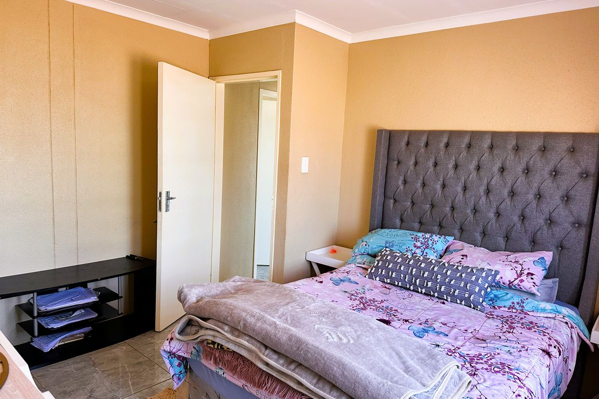 A functional bedroom featuring tiled flooring, neutral wall finishes, and a doorway leading to an adjacent space.