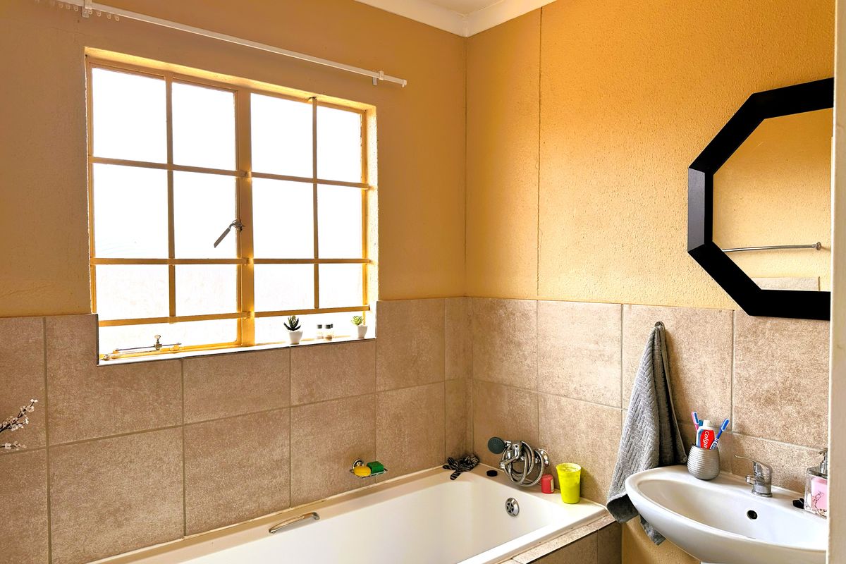 A functional bathroom featuring a built-in bathtub with tiled surround, a pedestal basin, and a window providing natural light.
