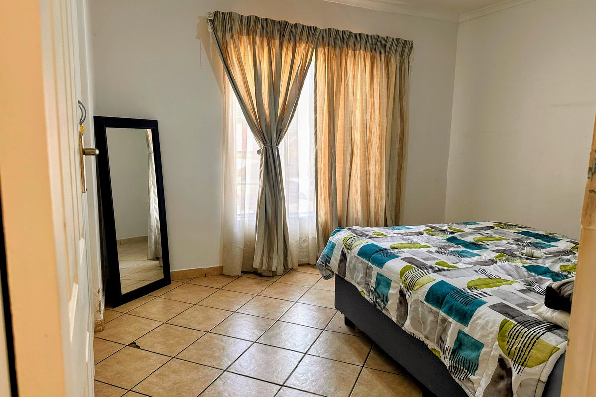 A bedroom featuring tiled flooring and a window with curtains, providing a functional and neutral living space.