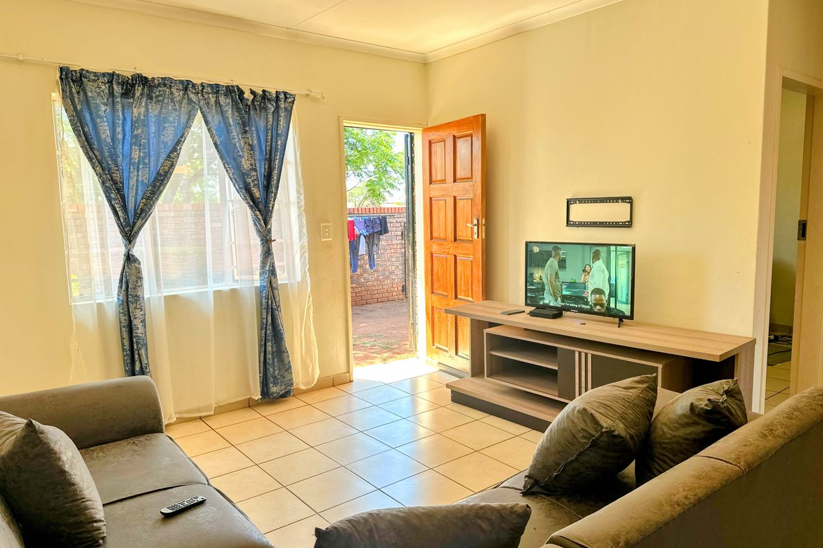A living room featuring tiled flooring, a wooden door leading to an outdoor area, and a window with natural light.