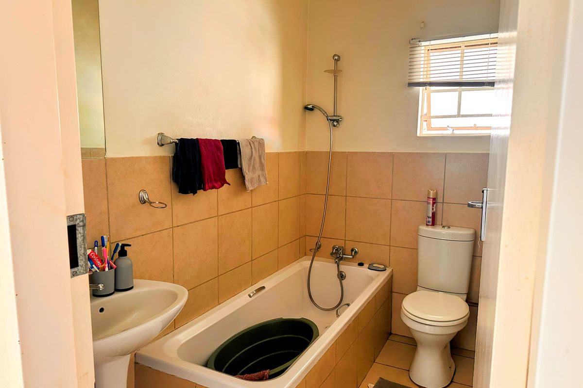 A functional bathroom featuring a pedestal basin, a bathtub with a handheld shower attachment, and a standard toilet with tiled walls.
