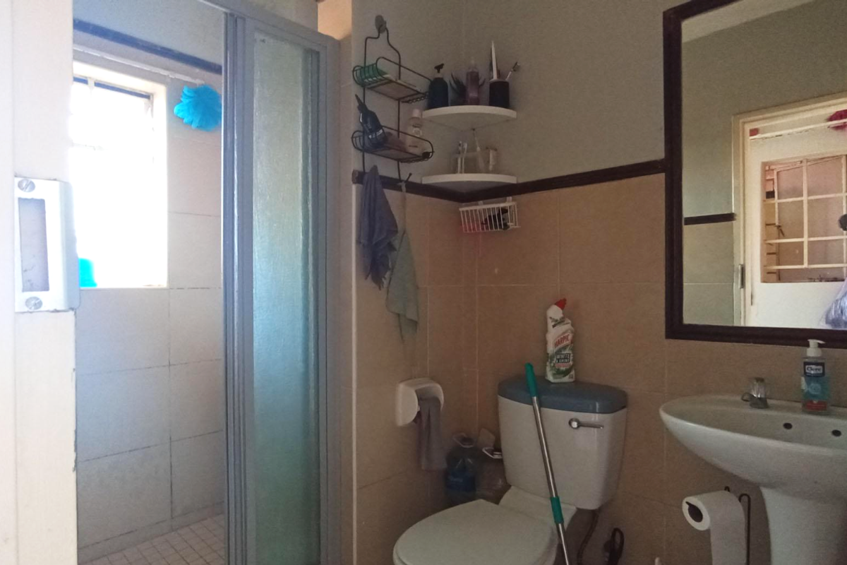 A functional bathroom featuring a pedestal basin, a toilet, and a glass-enclosed shower stall with tiled walls.