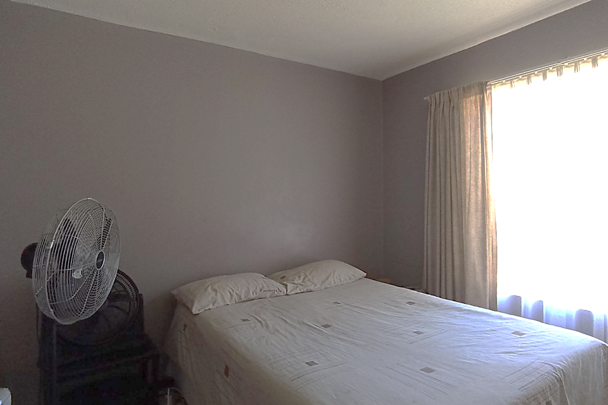 A standard bedroom featuring neutral wall tones and a large window with curtain treatments, providing natural light to the space.