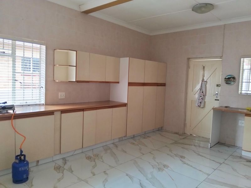 A functional kitchen featuring neutral built-in cabinetry, laminate countertops, and modern marble-look floor tiles, offering a clean and practical workspace.